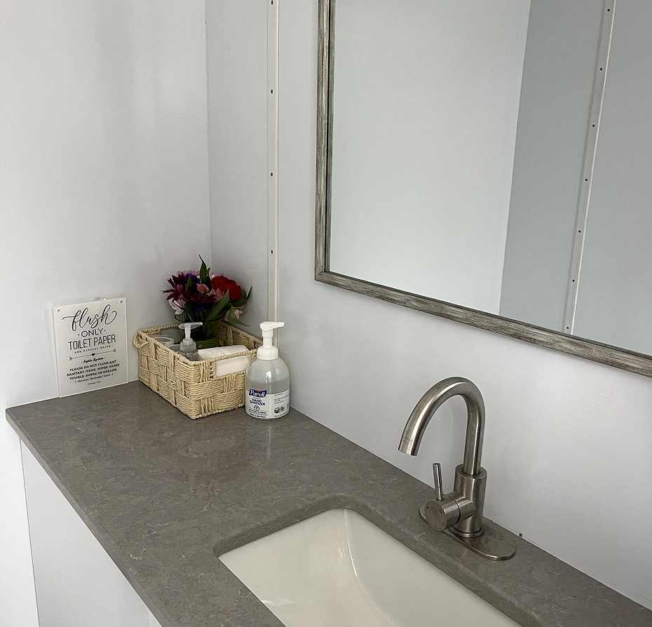 Bathroom sink with a tap, a platform with a basket containing a bottle and a flower vase