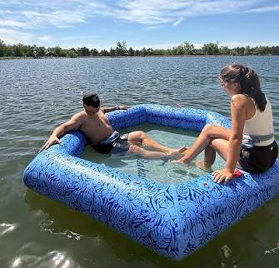 Man and woman sitting on an inflatable raft in the water, surrounded by trees and a clear blue sky