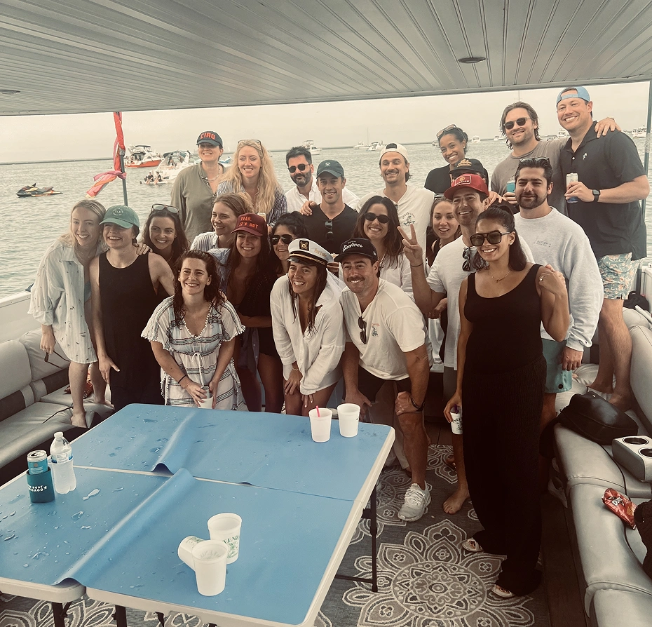 Group of people standing around a table on a boat, and enjoying a game of ping pong