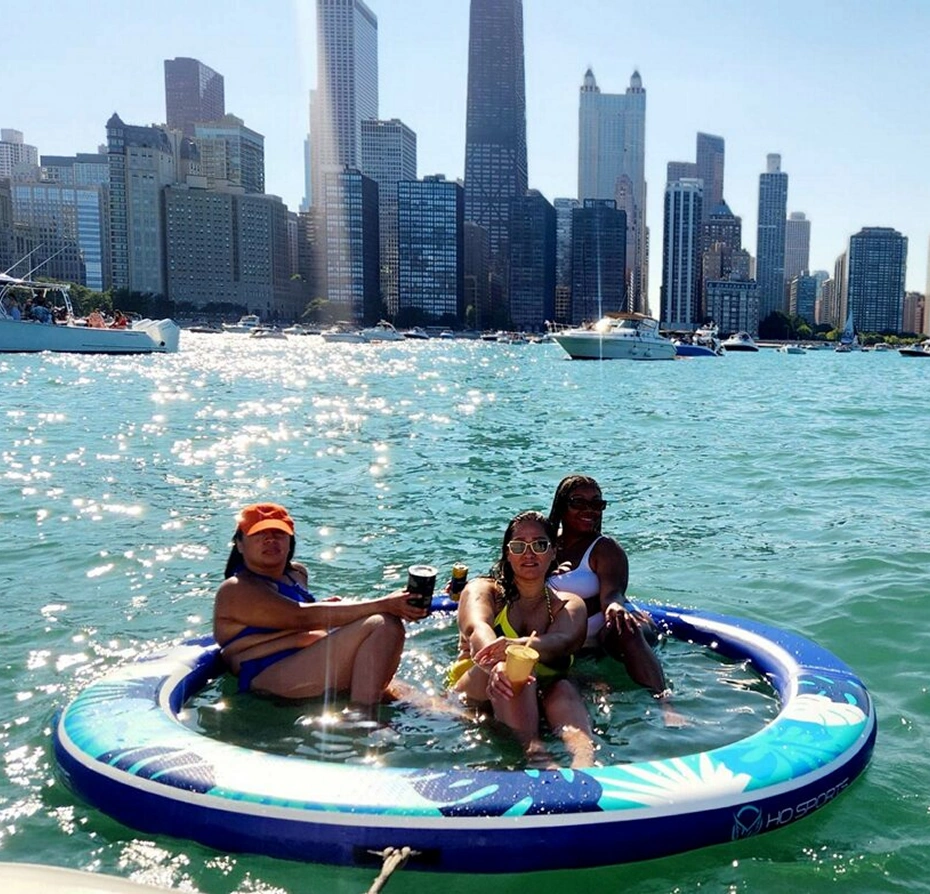 Three women sitting on an inflatable raft in the water with a city skyline in the background