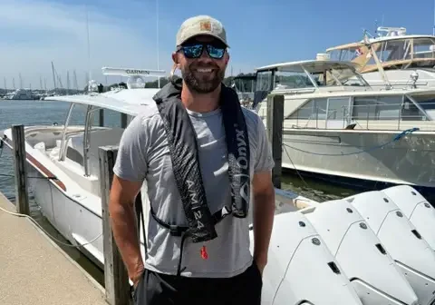 Man wearing a cap and goggles standing next to a boat in the water