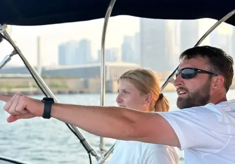 Man and woman on a boat in the water, with the man pointing at something