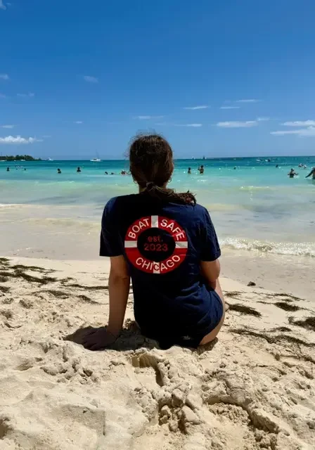 Woman sitting on the beach, looking out at the ocean with a few people in the water