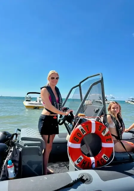 Woman standing on top of a boat in the water, with two other women sitting in the boat