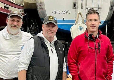 Three men standing in front of boats.