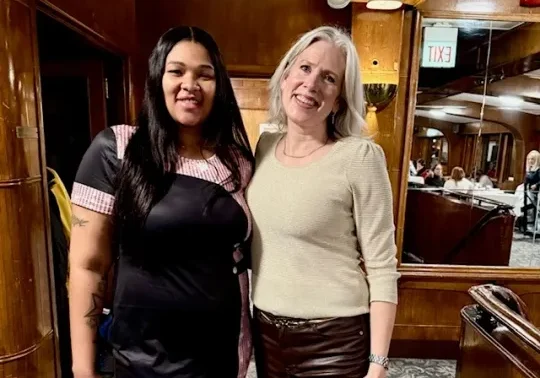 Two women posing together inside a wood-paneled boat cabin